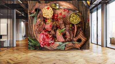 Overhead shot of kangaroo meat steak with green pesto and pomegranate on wooden cutting board. Healthy holiday food concept. Wall mural