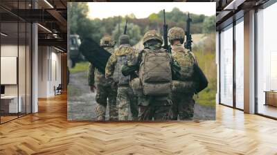 Military Personnel Walking on Rural Road. A group of military men returning after completing a task. Soldiers in military uniform with machine guns walk on a stony road with their backs to the cell. Wall mural