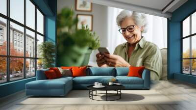 Portrait of an elderly woman sitting on a sofa at home. She uses her smartphone to send a text message or make a call. Wall mural