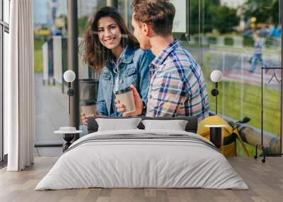 Positive relax couple traveler drinking coffee outdoor at stop while waiting tram, sits on bench at sunny morning. Wall mural