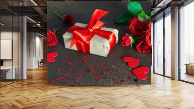 St. Valentine’s Day festive composition with gift box with big red bow, bouquet of red roses and shining decorations on dark rustic background. Wall mural