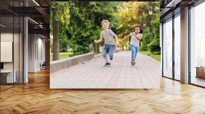 summer, childhood, leisure and people concept - happy little boy and girl playing tag game and running outdoors on green field Wall mural