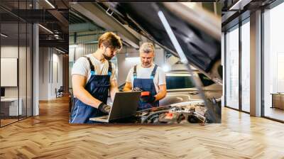 Team of two positive friendly car mechanics using a computer laptop to diagnosing and checking up on car engines parts for fixing and repair. Wall mural