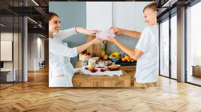 Teenage brother and her adult sister, young in 20s, fighting for sweet food at cozy home kitchen interior. Wall mural