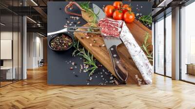 Traditional sausage cut into pieces with knife and fork with rosemary and spices on wooden cutting board . Wall mural