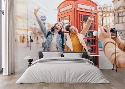 two friend, girlfriend and women using a mobile phone, camera and taking selfie against a red phonebox in the city of England.Travel Lifestyle concept Wall mural