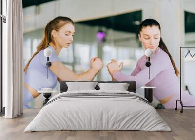 Two happy young caucasian female athletic people performing squat exercises face to face with friend at fitness gym. Group of two confident women with healthy lifestyle working out together. Wall mural