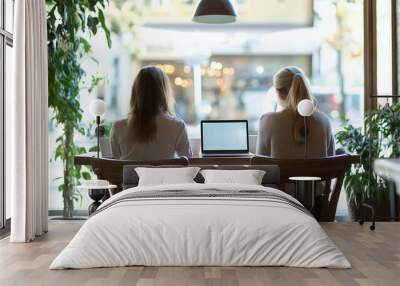 Two women sitting at a table with laptops in front of them. One of the women is wearing a white shirt Wall mural