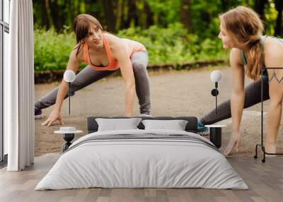 Two young woman doing stretching exercises in summer park before running. Morning, healthy lifestyle concept Wall mural