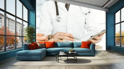 Unknown male doctor and woman-patient discussing current health examination while sitting in clinic and using clipboard. Good medical service in hospital. Medicine concept Wall mural