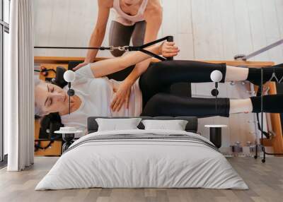 Woman practicing stretching exercise on reformer in gym Wall mural