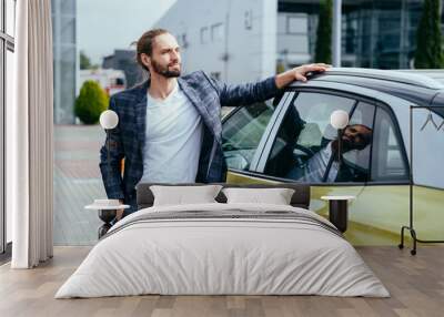 Young elegant fashionable man wearing plaid suit leaning on his car outdoor. Wall mural