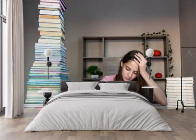 Young girl studying with tall stacks of books. A young girl sitting at a desk with two large stacks of books on either side, reading intently. Wall mural