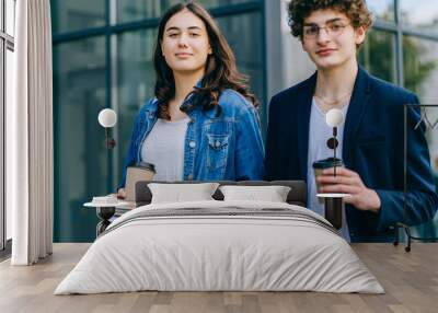 Young woman and man having fun together after classes, drinking coffee and having good time. Students in love holding books, exercise books, spend time together after attending lectures and seminars Wall mural