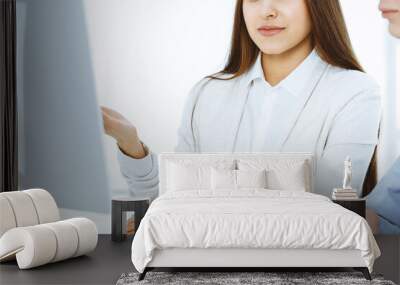 Young woman sitting at the desk with computer in white colored office. Looks like student girl or business lady communicating with casual dressed man Wall mural