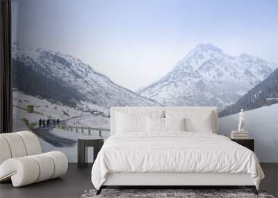 A group of people walking on an icy road in winter with the snow-capped mountains in the background at Vall Incles, Andorra Wall mural