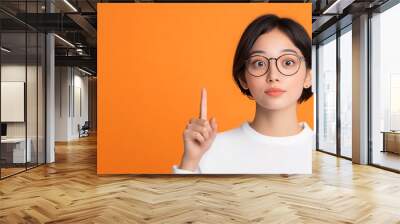 Japanese woman pointing up, idea expression pose, advertisement pose, orange background. Wall mural