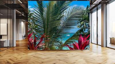 Tropical garden view at an all-inclusive resort in Nungwi, Zanzibar, Tanzania. Palm fronds and vibrant red foliage with turquoise sea and clear blue sky in the background. Wall mural