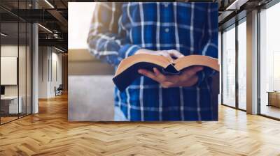 a man standing while reading bible or  book over concrete wall with window light  Wall mural