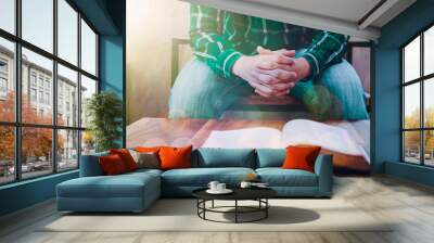 Close up of a man hands praying to God while sitting on wooden chair wirh blur open bible in the office Wall mural