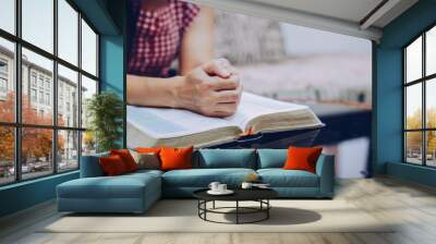 Close up of a woman hands praying on the open holy  bible on a table indoor with the windows light lay warm tone . Christian faith and trust concept  with copy space. Christian devotional background. Wall mural