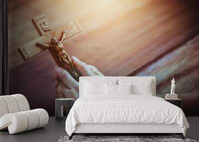 Close up of human hand holding the crucifix of Jesus Christ with the sun light on wooden table Christian believe , trust or easter concept Wall mural