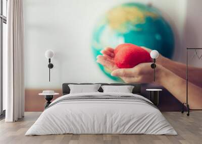 Close up of woman hands holding red heart over blurred world globe on wooden table , christian mission and peaceful concept, earth day background. Copy space Wall mural