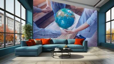 Three people standing and holding hands each other while pray to God for the world with blurred world globe on wooden table, Christian background for great commission or earth day concept. Wall mural