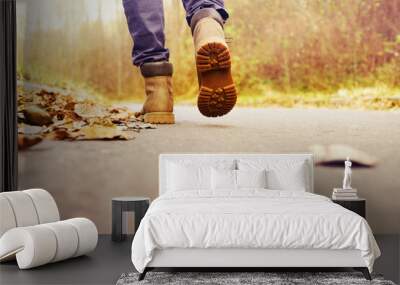 Feet in brown leather boots are walking along the road on an autumn day, close up, back view, soft focus Wall mural