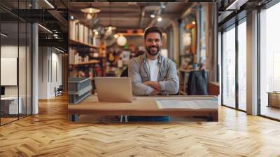 Happy Caucasian young male freelancer smiling while working in the laptop and seated in a charming place, vintage lighting interior, smiling boy wearing casual dress and looking at camera Wall mural