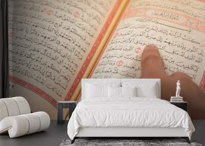 Quran (Koran) - close up of holy book of Muslims, with hand pointing ayat (Āyah), and shining light. Wall mural