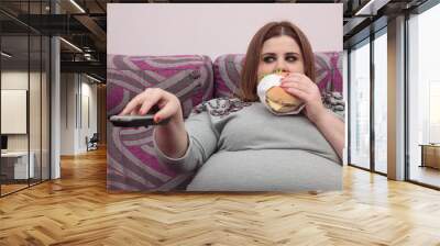 Overweight woman eating a burger and watching tv Wall mural