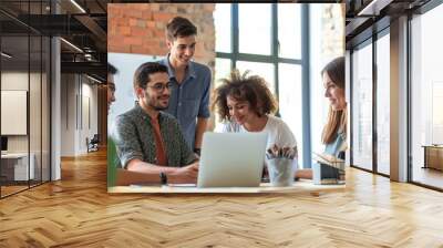 A diverse team of young adults engaging in a meeting with a laptop in a bright, modern office, conveying a dynamic and collaborative work atmosphere. Wall mural