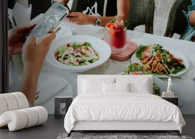 People enjoying a meal together at a restaurant, with one person taking a photo of their food, suitable for social media or dining promotions. Wall mural