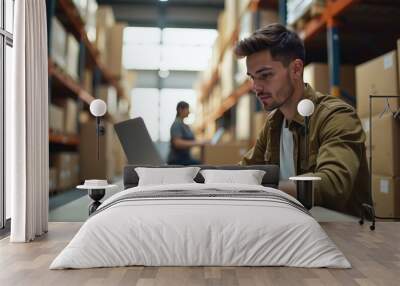 Young Man Working on Laptop in Warehouse, Inventory Management Concept. Wall mural