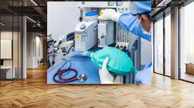 Anesthesiologist or doctor in blue gown working with anesthetic machine inside operating room in hospital.Right hand control machine with ambu bag.Medical device for surgery.Gas exchange control. Wall mural