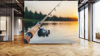 A fishing rod rests by a serene lake at sunset, capturing a moment of leisure and nature. Wall mural