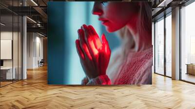 A woman with her hands clasped together in prayer, illuminated by a soft red glow. The image evokes a sense of hope, faith, and spirituality. Wall mural