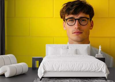 Young man wearing glasses and a white shirt standing in front of a yellow wall. Wall mural