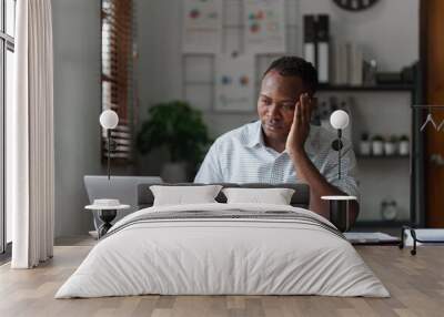 Tired American African business man in stress works with many paperwork document. migraine attack. Freelance, work from home Wall mural