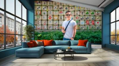 A young happy Latino man smiling in front of decorative sake barrels at Meiji Shrine in Tokyo, Japan, looking happy. Wall mural