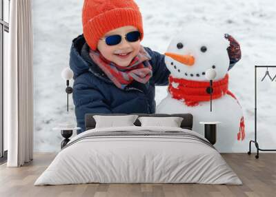 Child playing with snowman in winter, smiling in a snowy landscape. Wall mural