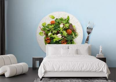 Healthy green salad on white plate with fresh salad leaves, tomatoes and mozzarella cheese on blue background Wall mural