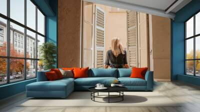 Blond hair woman in beautiful dress near the window with shutters. The beginning of a new day. Happy morning in Italy. Pretty girl in home. Enjoy moment, relax lifestyle. Cozy sunny day. Weekend vibes Wall mural