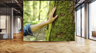 Girl hand touches a tree with moss in the wild forest. Forest ecology. Wild nature, wild life. Earth Day. Traveler girl in a beautiful green forest. Conservation, ecology, environment concept Wall mural