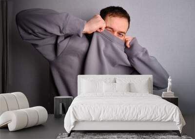 Man poses near a light wall in a gray sweatshirt. Gestures. Emotion. Casual wear. Studio model at work. Place for inscriptions and logo Wall mural