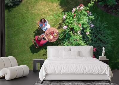 Young couple enjoying food and drinks in beautiful roses garden on romantic date, aerial top view from above of man and woman eating and drinking together outdoors in park Wall mural