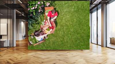 Young couple enjoying food and drinks in beautiful roses garden on romantic date, aerial top view from above of man and woman eating and drinking together outdoors in park
 Wall mural