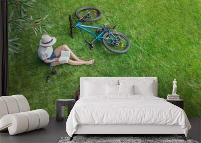 Young girls with bicycle in park, using laptop computer and headphones, two student girls studying online outdoors sitting on grass near bike, aerial drone view from above
 Wall mural