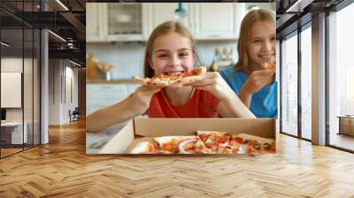 Two happy young girls eating pizza in the kitchen at home Wall mural